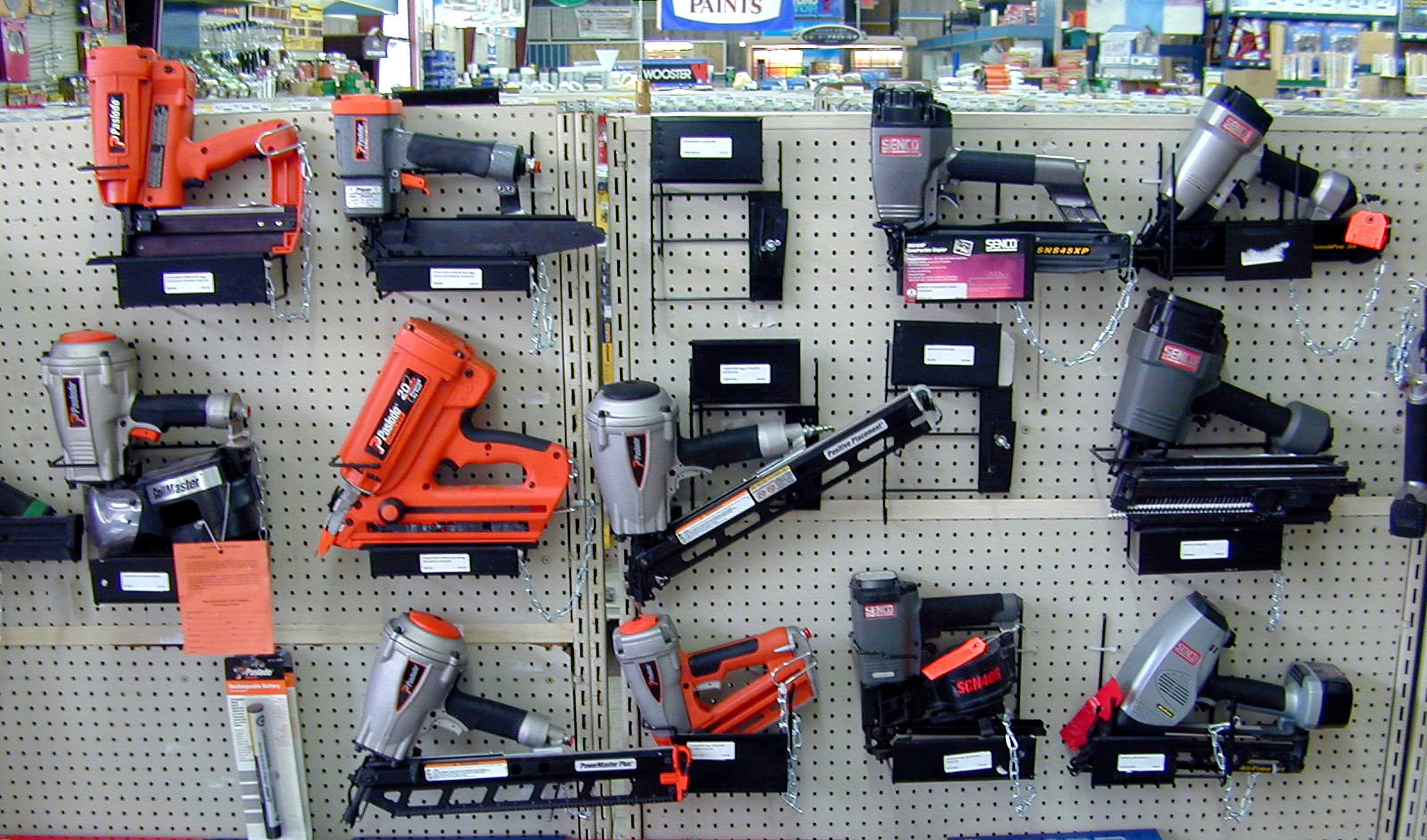 Pneumatic nail guns and finish nailers on pegboard with manufacturer boxes below
